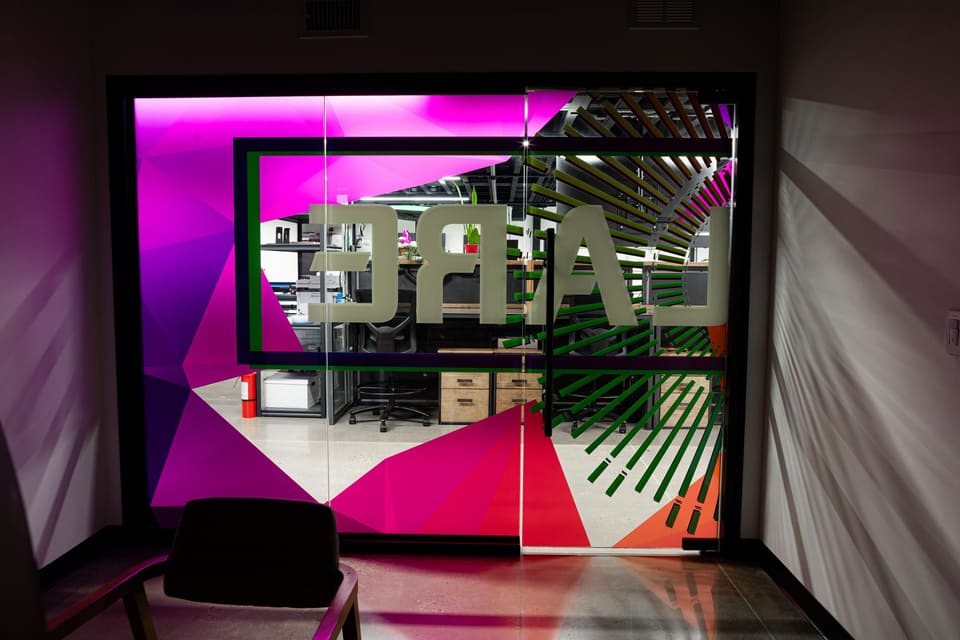 Glass-walled studio room with a magenta and green geometric print and large mirrored lettering
