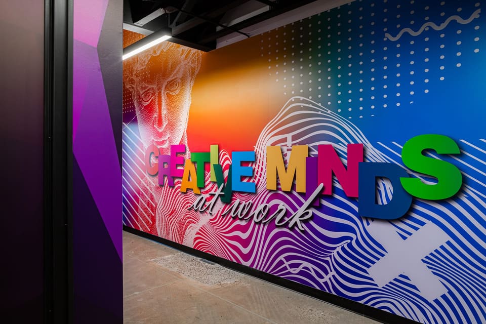 Studio wall with a flowing blue and orange wave print, a classical sculpture graphic and dimensional colored letters