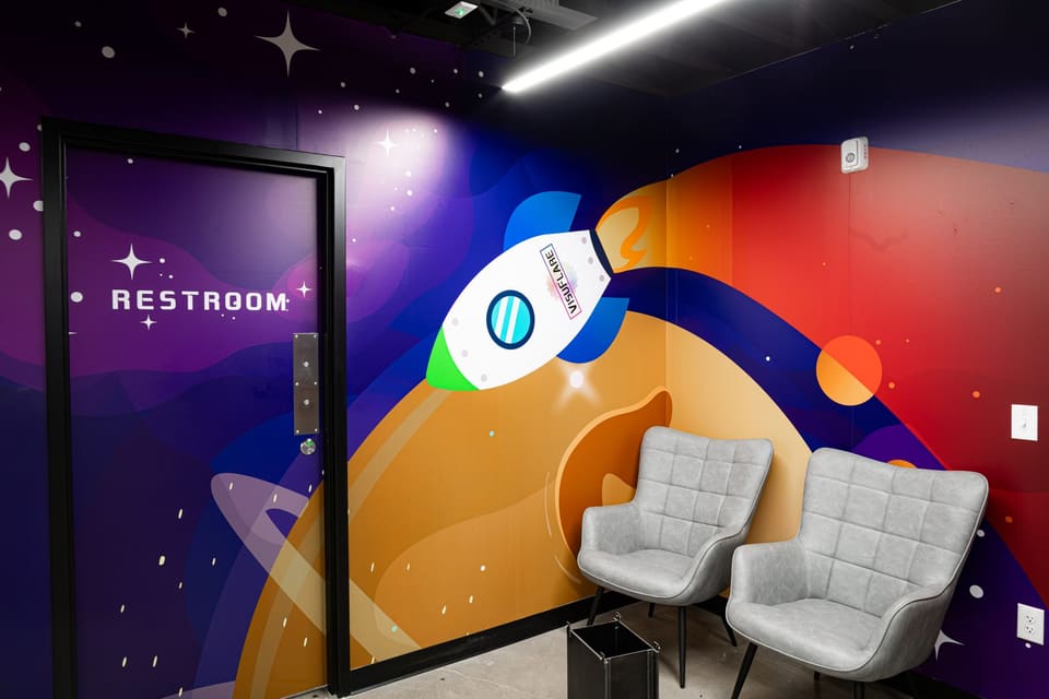 Restroom door and a space-themed wall mural with a rocket and planet, with two gray chairs