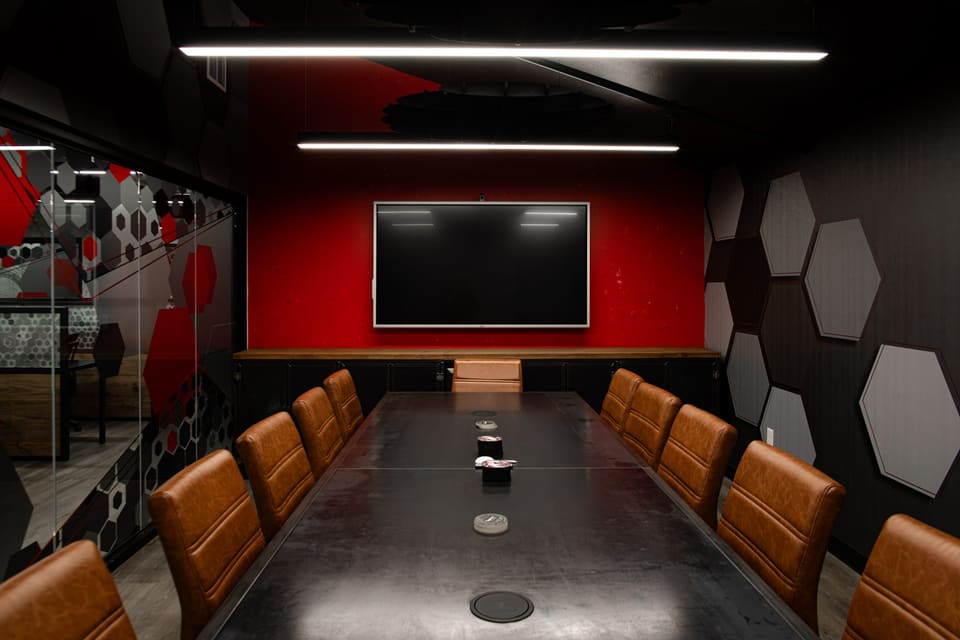 Conference table and leather chairs facing a red wall with a display, with patterned glass on the left