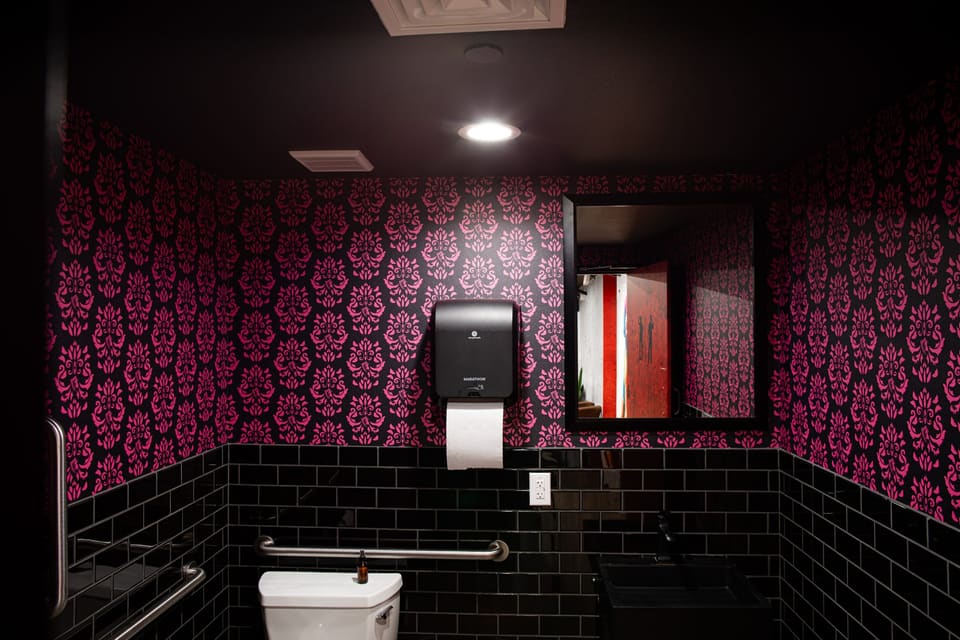 Restroom with pink and black damask wallcovering above black subway tile