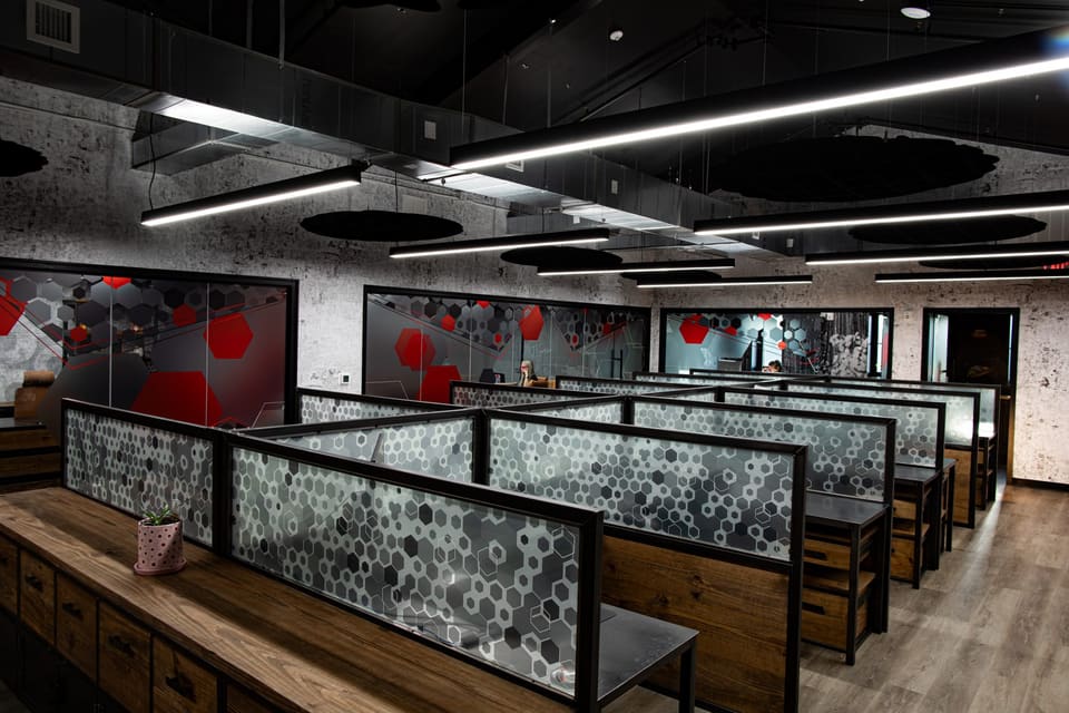 Open office from the end of a bench desk showing rows of workstations and glass offices beyond