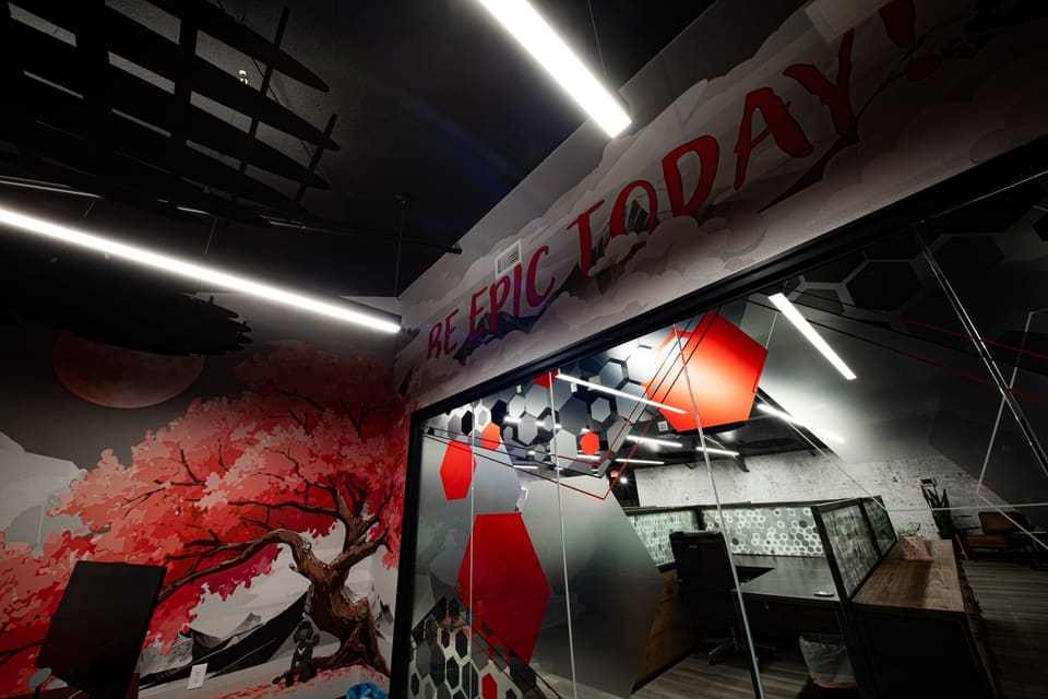 Office corner with a red and white tree mural on the wall and large lettering across the upper wall, beside a glass partition