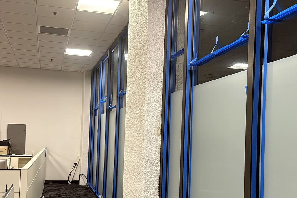 Office glass with blue painter’s tape along the frame and a frost band at desk height, work in progress