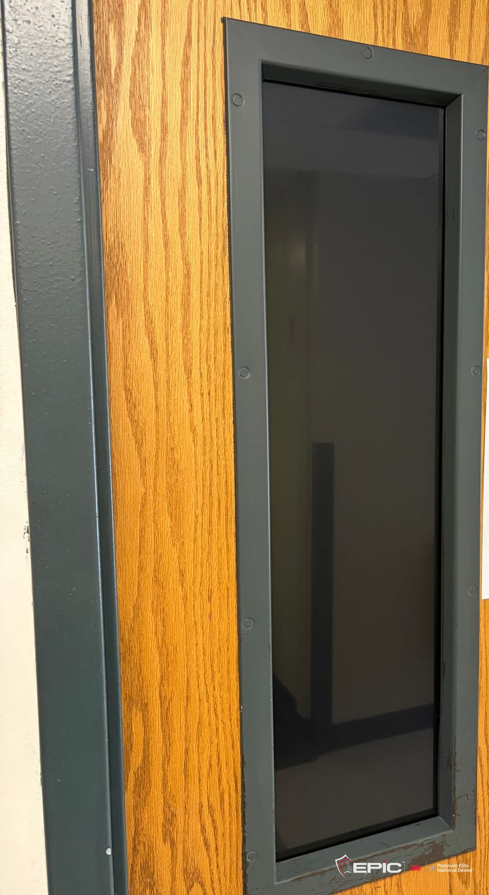 A classroom door lite covered edge to edge in dark blackout film, the frame edge clean, dark from the corridor