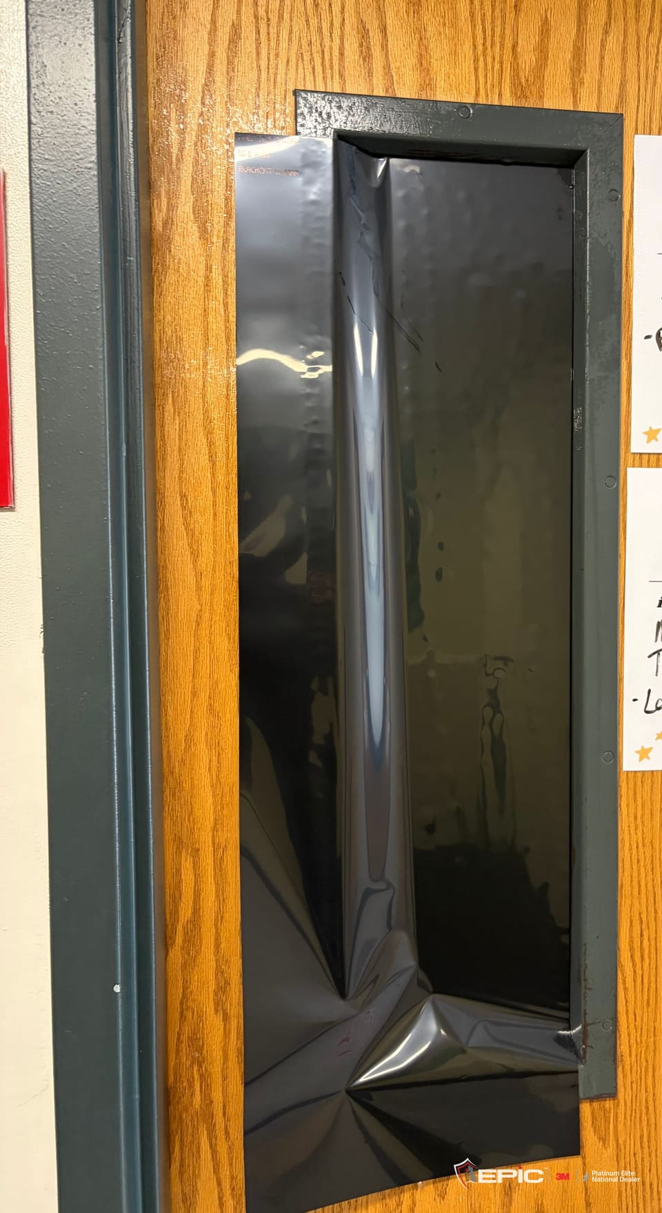 A classroom door lite with a sheet of blackout film laid on, edges still to trim