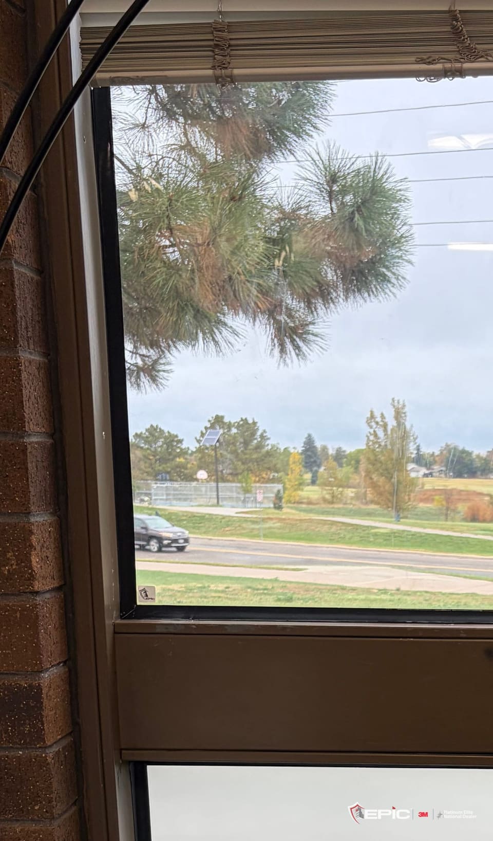 A classroom window in a brick wall: the upper lite clear with trees and a field beyond, the lower lite finished in white 3M Privacy Matte frost