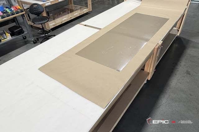 A cut sheet of security film lying on kraft paper on a long packaging table, racks of boxed film behind