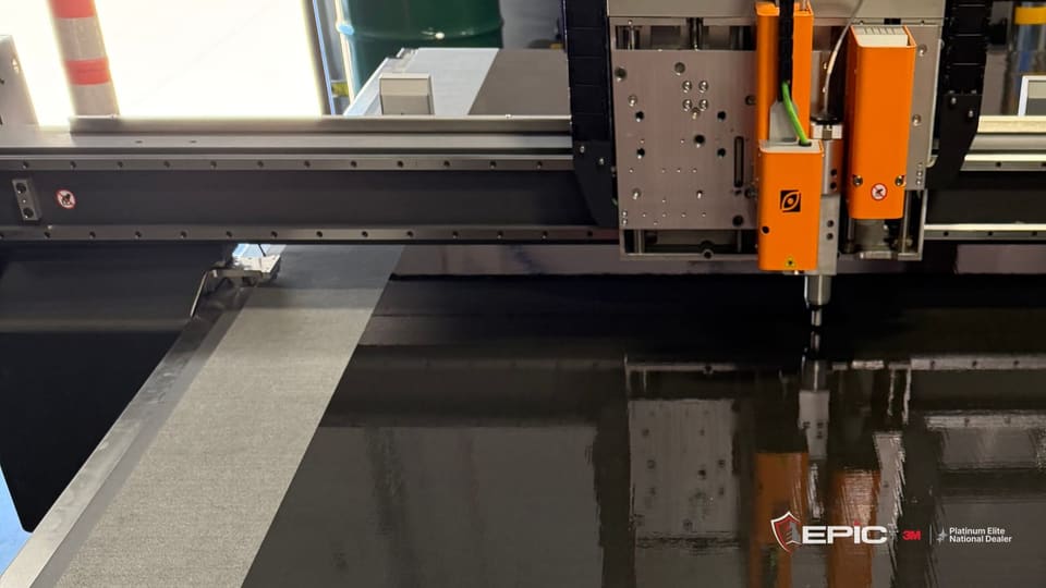 A long sheet of clear solar film laid out across the cutting table in Epic's Aurora facility, the cutting head at the far end
