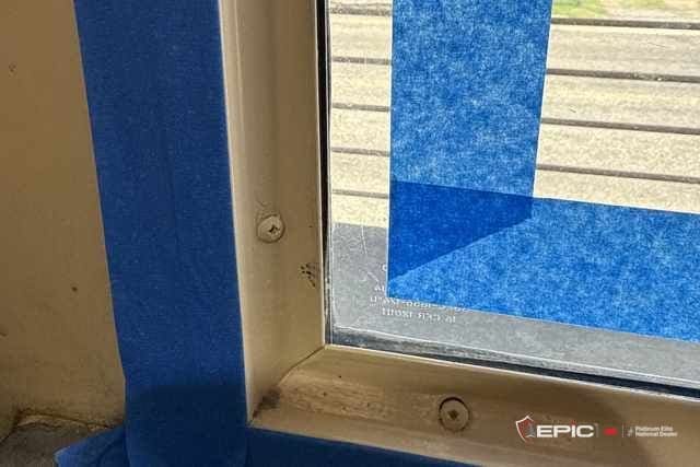 Frame corner at a Belton ISD school with blue tape on the jamb and sill and a taped line on the glass