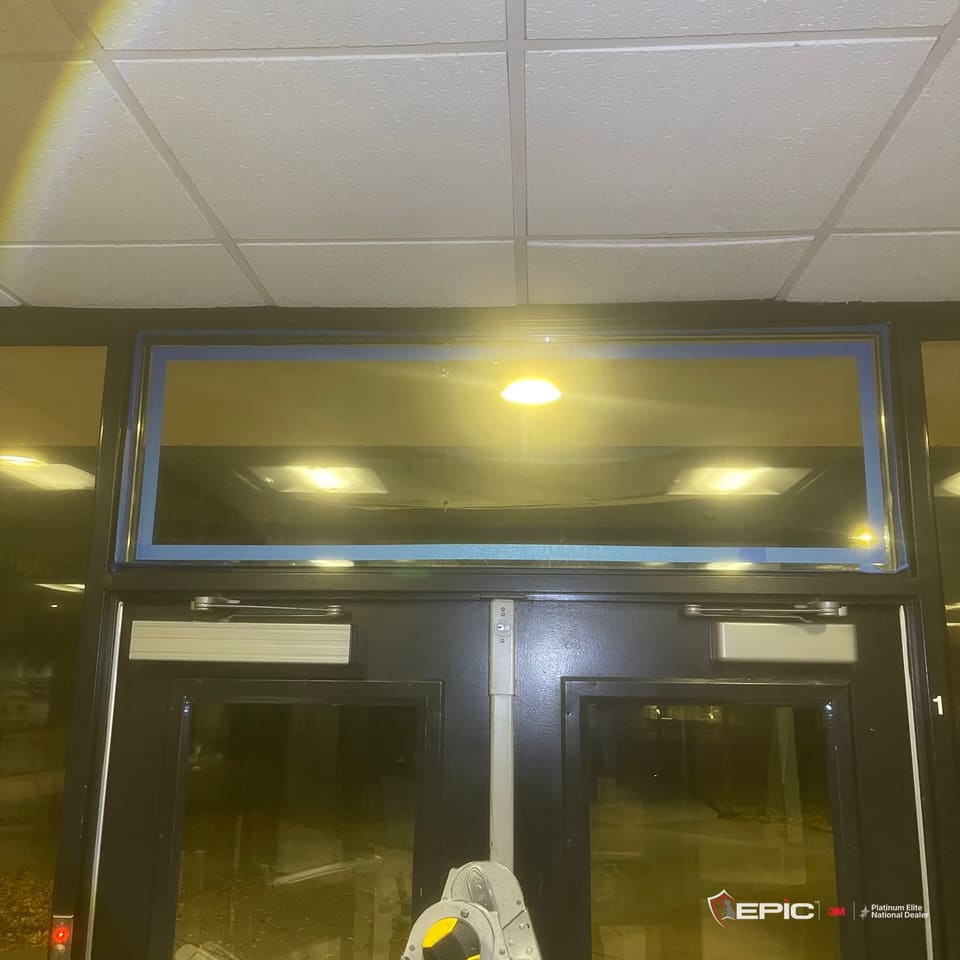 The transom over a pair of school entry doors at night, the film on and every edge of the frame taped in blue