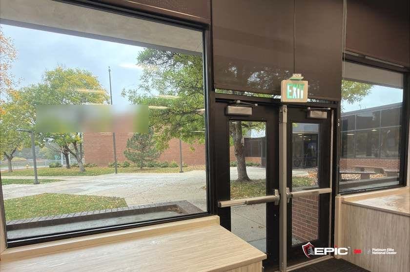Entry 10 exit doors with the EXIT sign and panic bars, filmed lites either side, brick school building outside