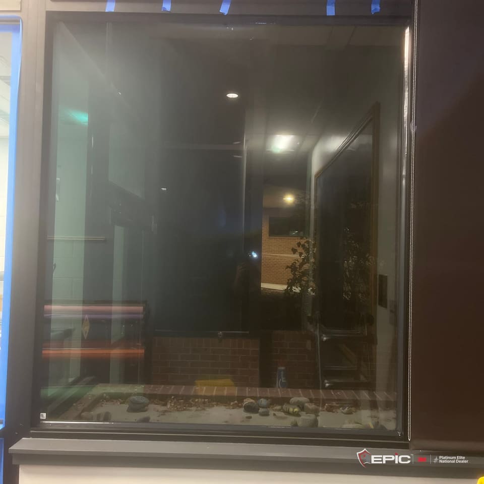 A hallway window at a Cherry Creek school taped in blue on every edge of the frame, the courtyard dark beyond the glass