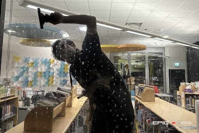 Silhouette of a Certified Installation Specialist squeegeeing solution from a glass wall in a lit school library after hours