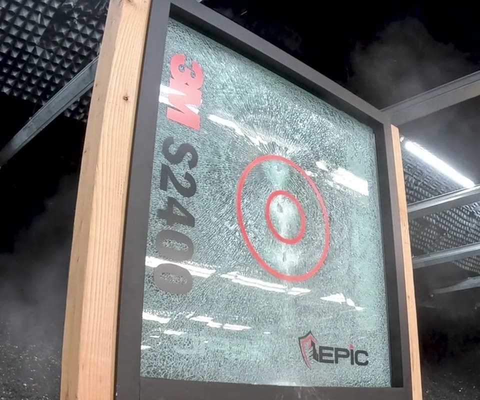 After: 3M S2400 security film test panel on a wooden stand at Epic’s live demonstration, before and after the impact sequence — the glass shattered but held in the frame