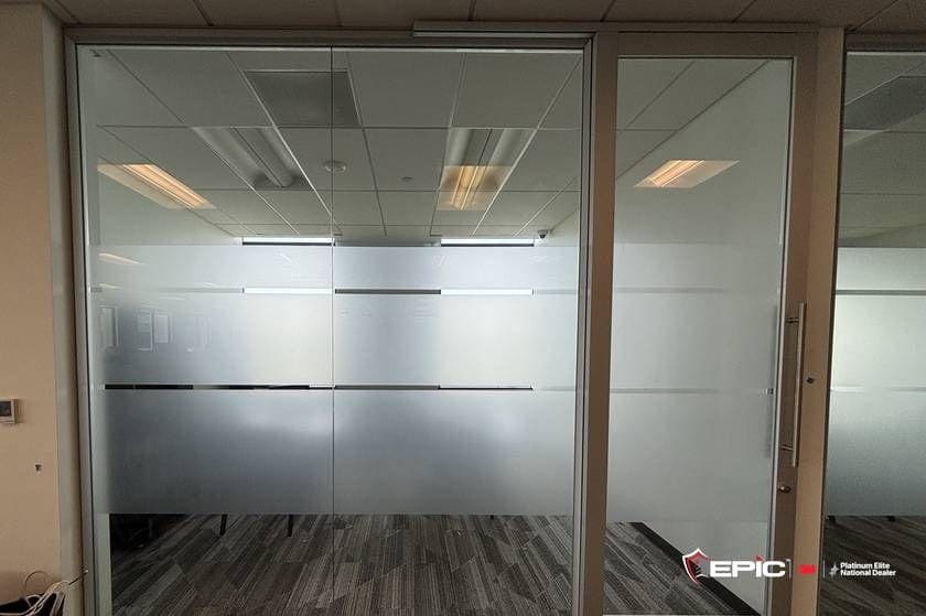 A glass office front and door with a custom frost pattern: a wide frosted field with thin clear horizontal reveals, ceiling and carpet visible through the clear bands