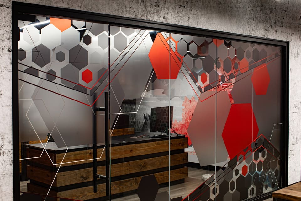 Glass office wall with red and gray hexagon frosted graphics and a wood desk behind
