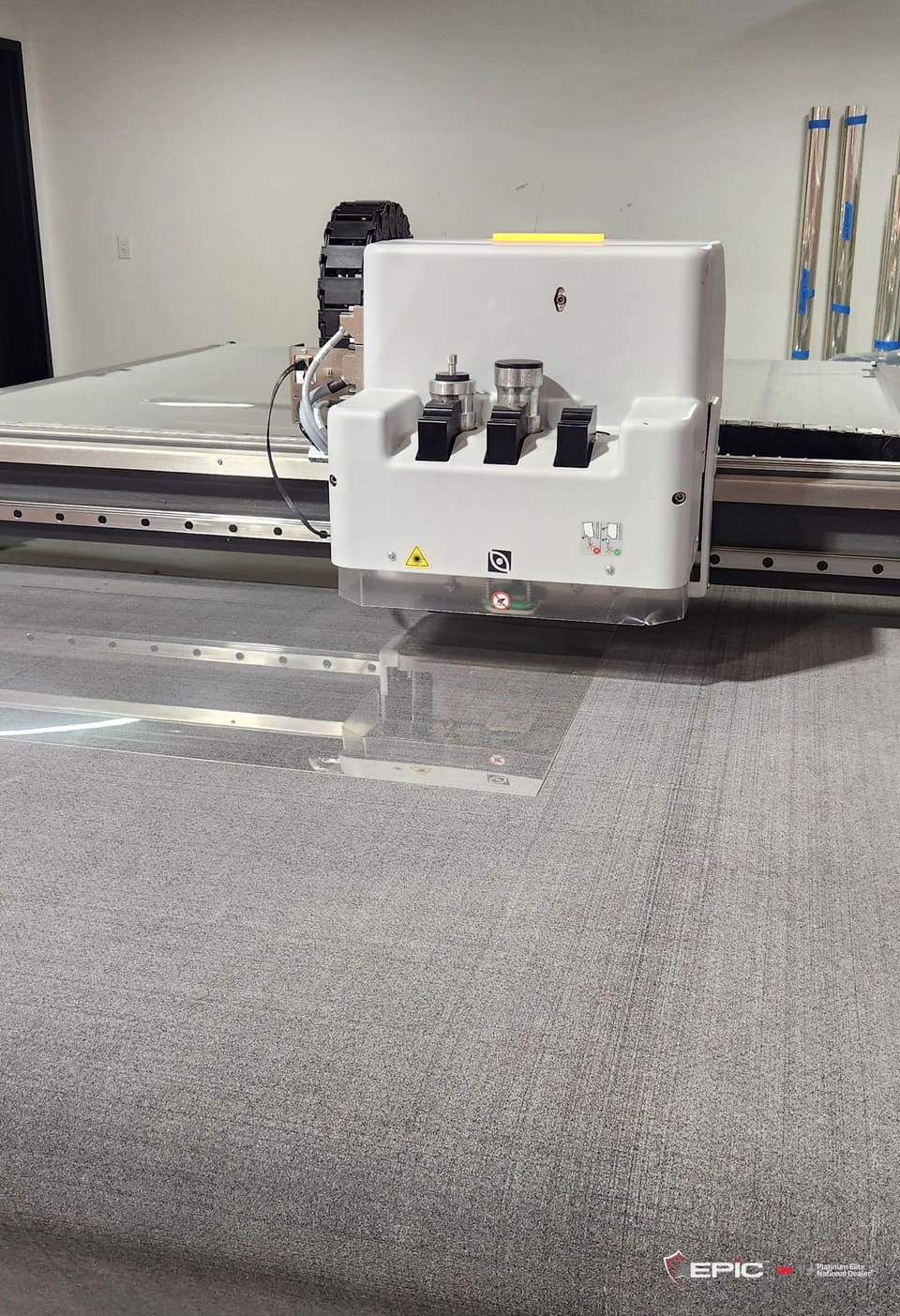 The Epic Precision cutting head over a cut sheet of 3M S2400 on the bed at Epic's McKinney shop, banded rolls of film against the wall