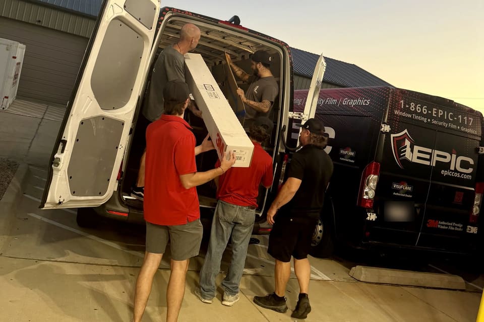 Crew loading a boxed roll of 3M film into the van