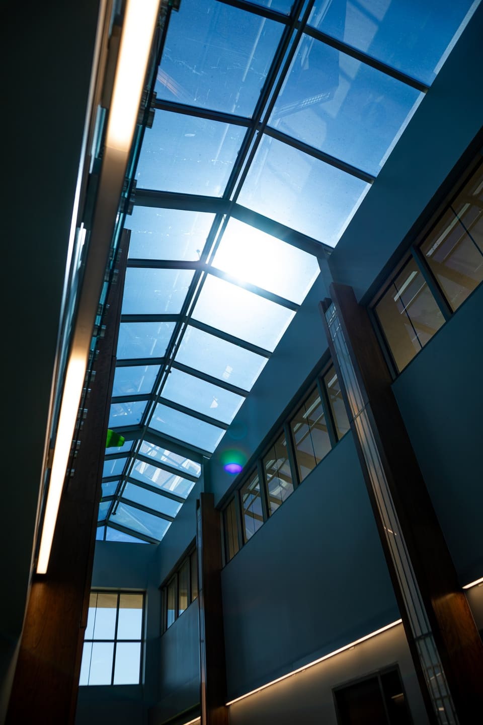 Looking straight up through the atrium skylight, sun breaking through the glass between the frames