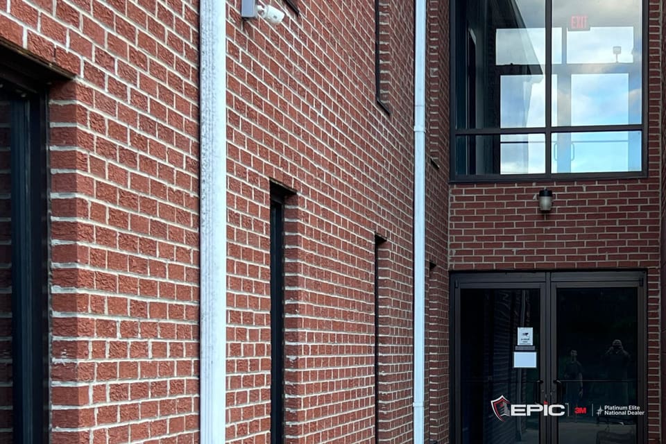 Dark bronze double doors with glass and a transom above them in a brick alcove, narrow punched windows to the left