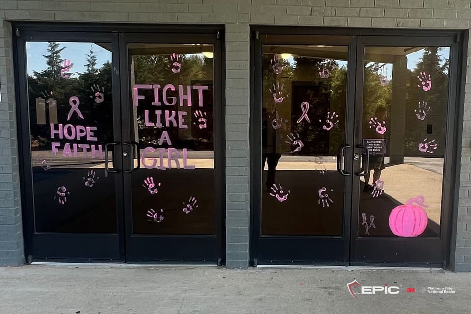 Two pairs of black aluminum entry doors with dark glass, pink painted handprints and ribbons across the panes