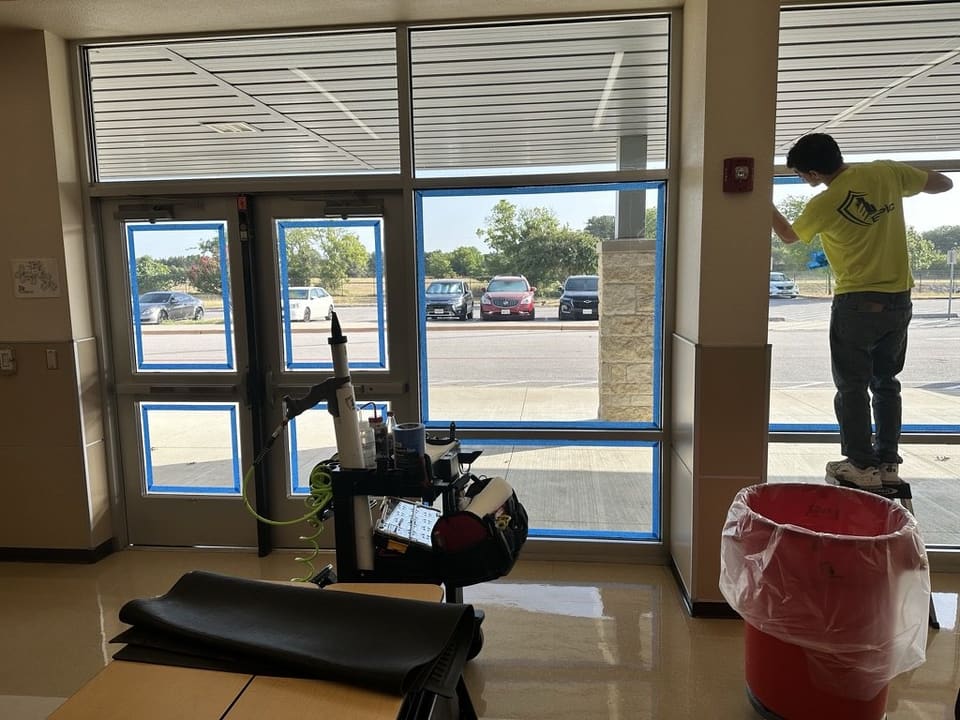 Certified Installation Specialist on a step stool setting blue tape around the frame of a cafeteria window