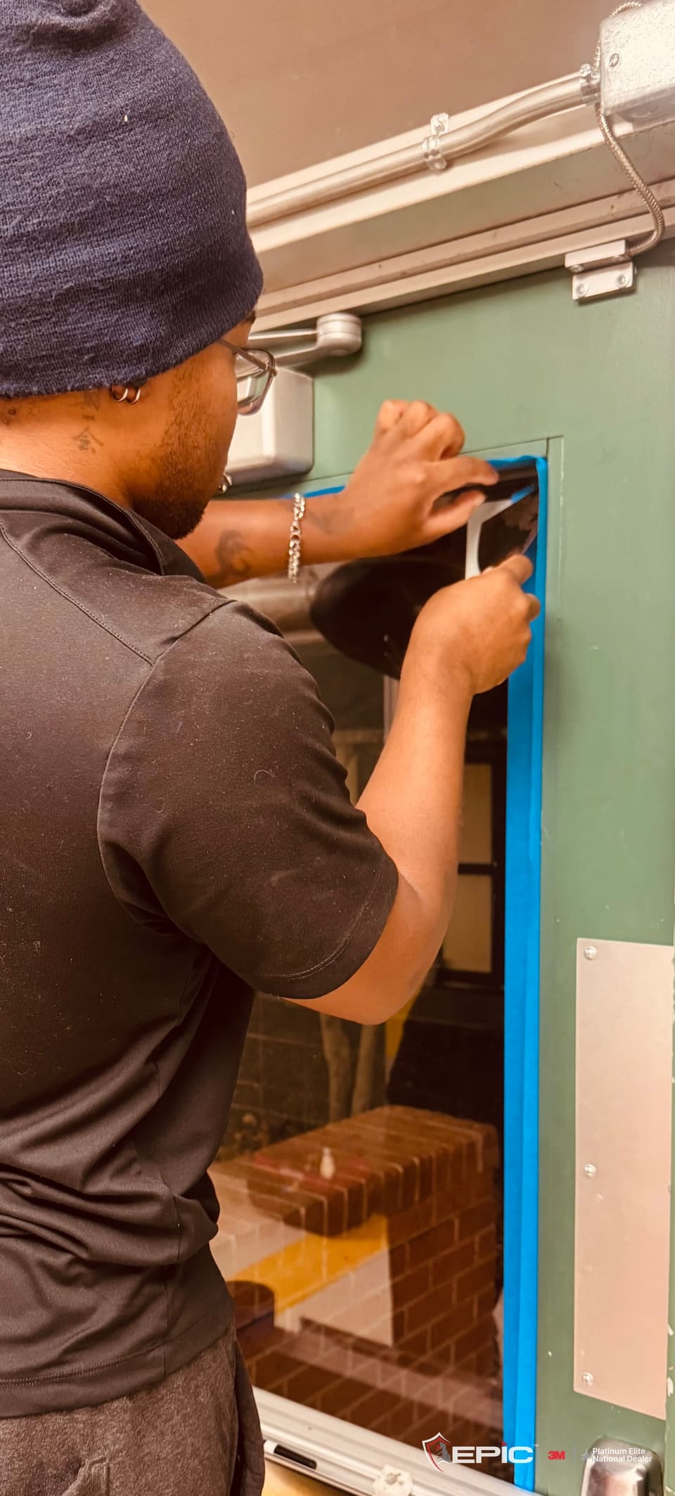 A Certified Installation Specialist pressing blue tape down the edge of a green door's lite at a Dallas ISD school