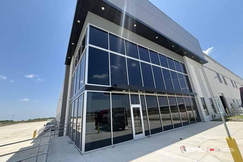 Two stories of dark, filmed curtain-wall glass at the corner of a new distribution building under a blue sky